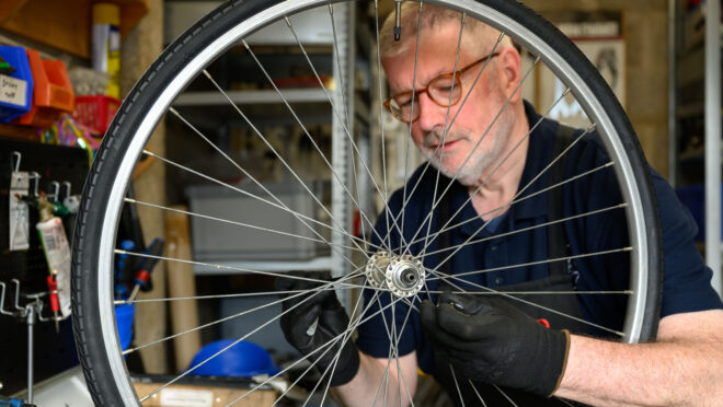 A man repairing a bike heel. The man is behind the wheel and the wheel takes up most of the pictures.