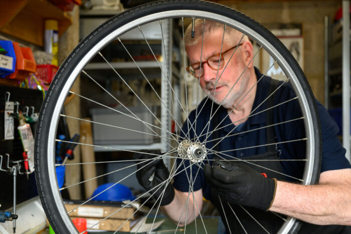 A man repairing a bike heel. The man is behind the wheel and the wheel takes up most of the pictures.
