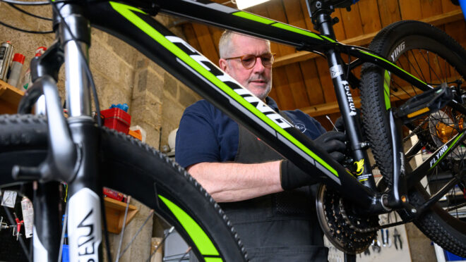 A mam fixing a black and green bike in a workshop