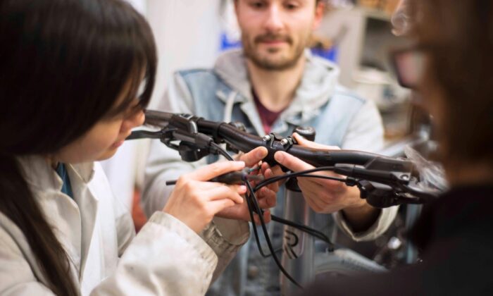 Close-up of people adjusting a bicycle’s handlebars and brake cables during a repair session.