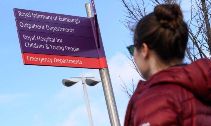 Person in a red jacket looking at a hospital direction sign for the Royal Infirmary of Edinburgh.